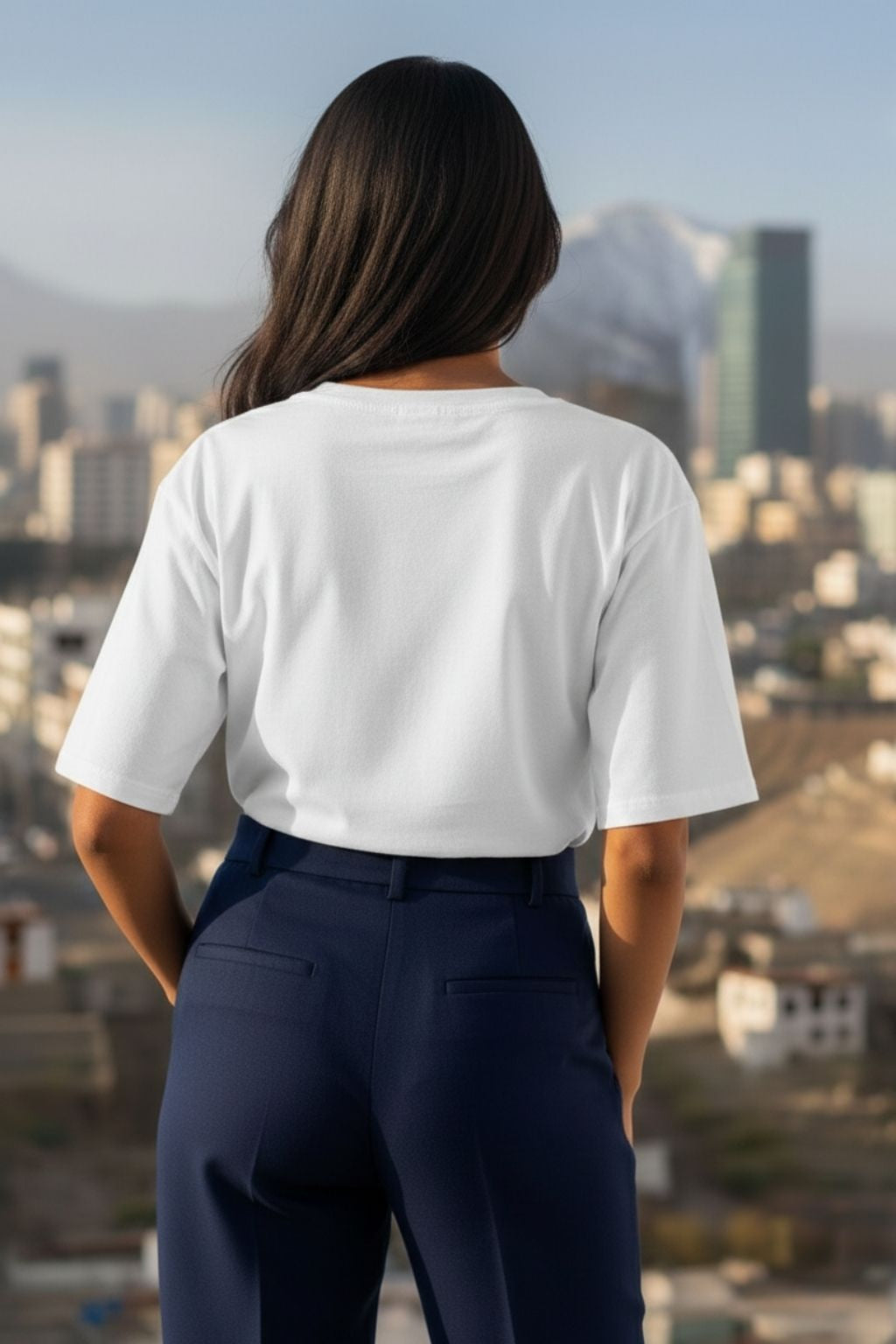 back view of a woman wearing a white oversized t-shirt and dark pants with a cityscape in the background