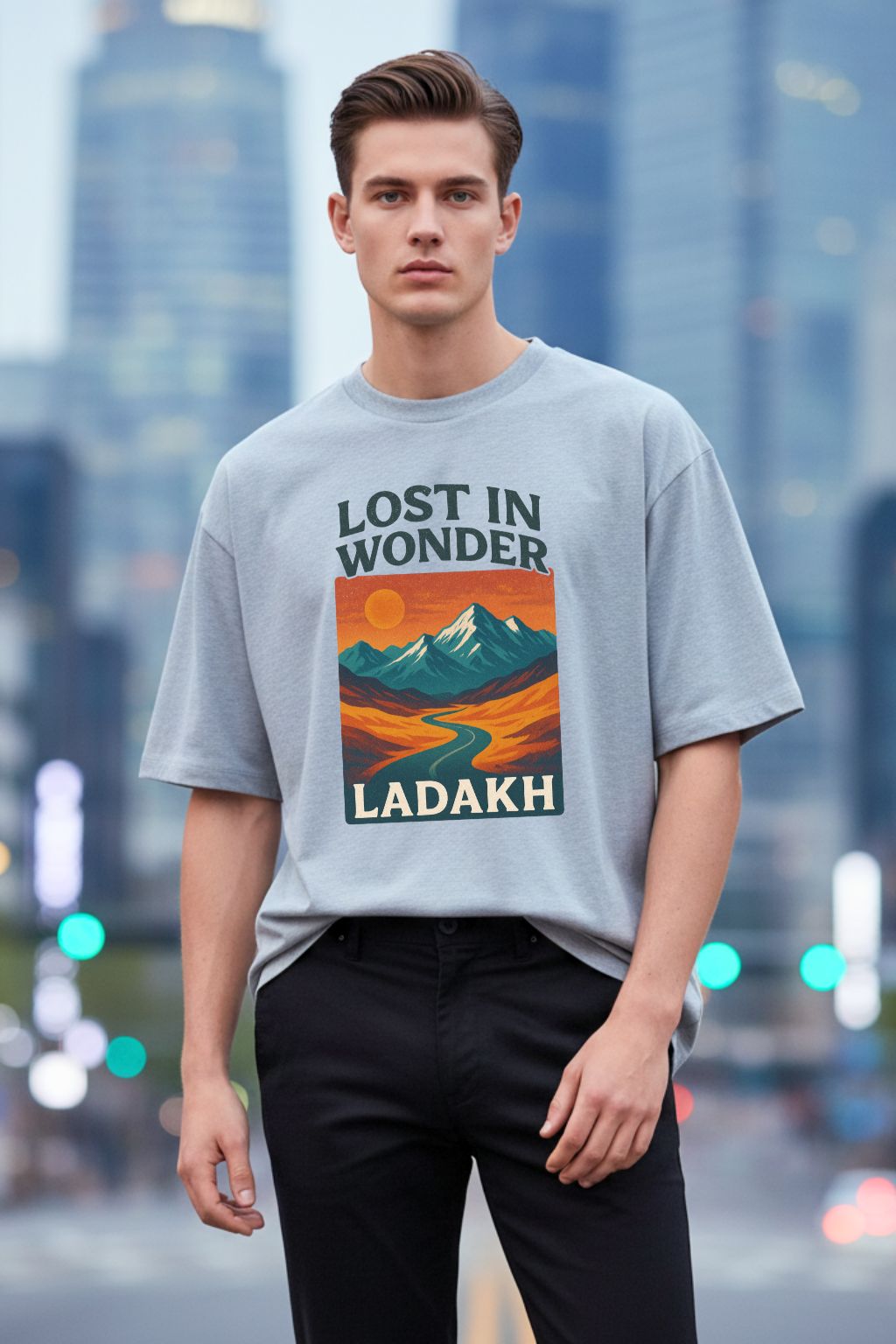 Man wearing a grey melange oversized t-shirt with 'Lost in Wonder Ladakh' design against a cityscape background