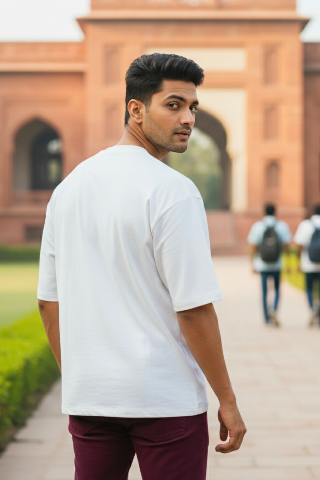 back view of a man in a white oversized t-shirt and maroon pants standing in front of a historical building.