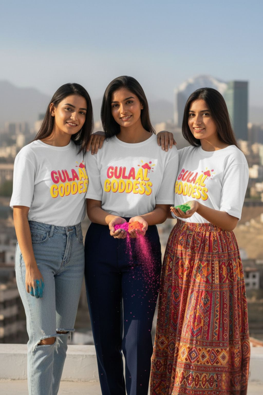 Three women wearing white oversized  'Gulaal Goddess' t-shirts with a cityscape in the background.