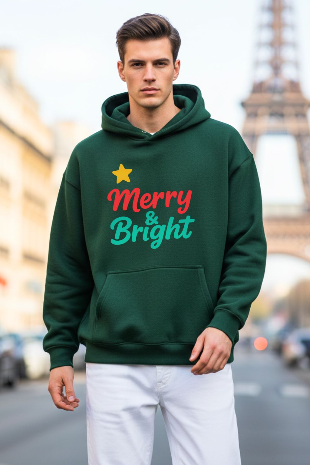 Man wearing a bottle green oversized hoodie with 'Merry & Bright' text in front of the Eiffel Tower.