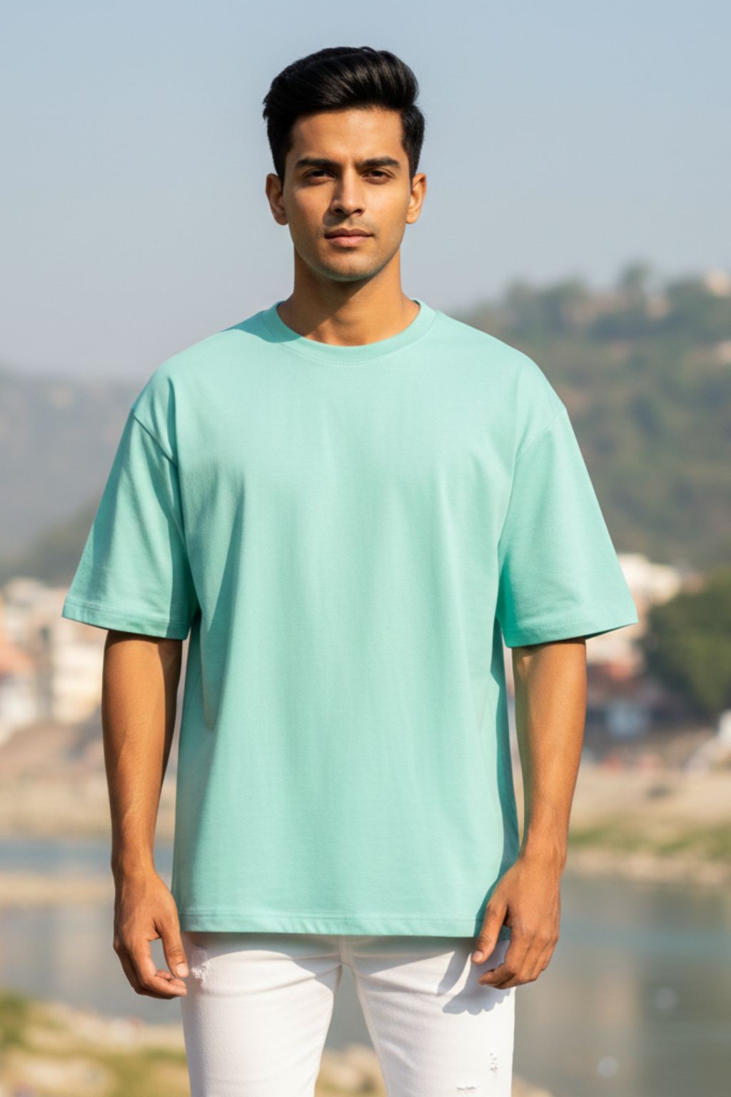 Man wearing a mint oversized t-shirt standing outdoors with a scenic background