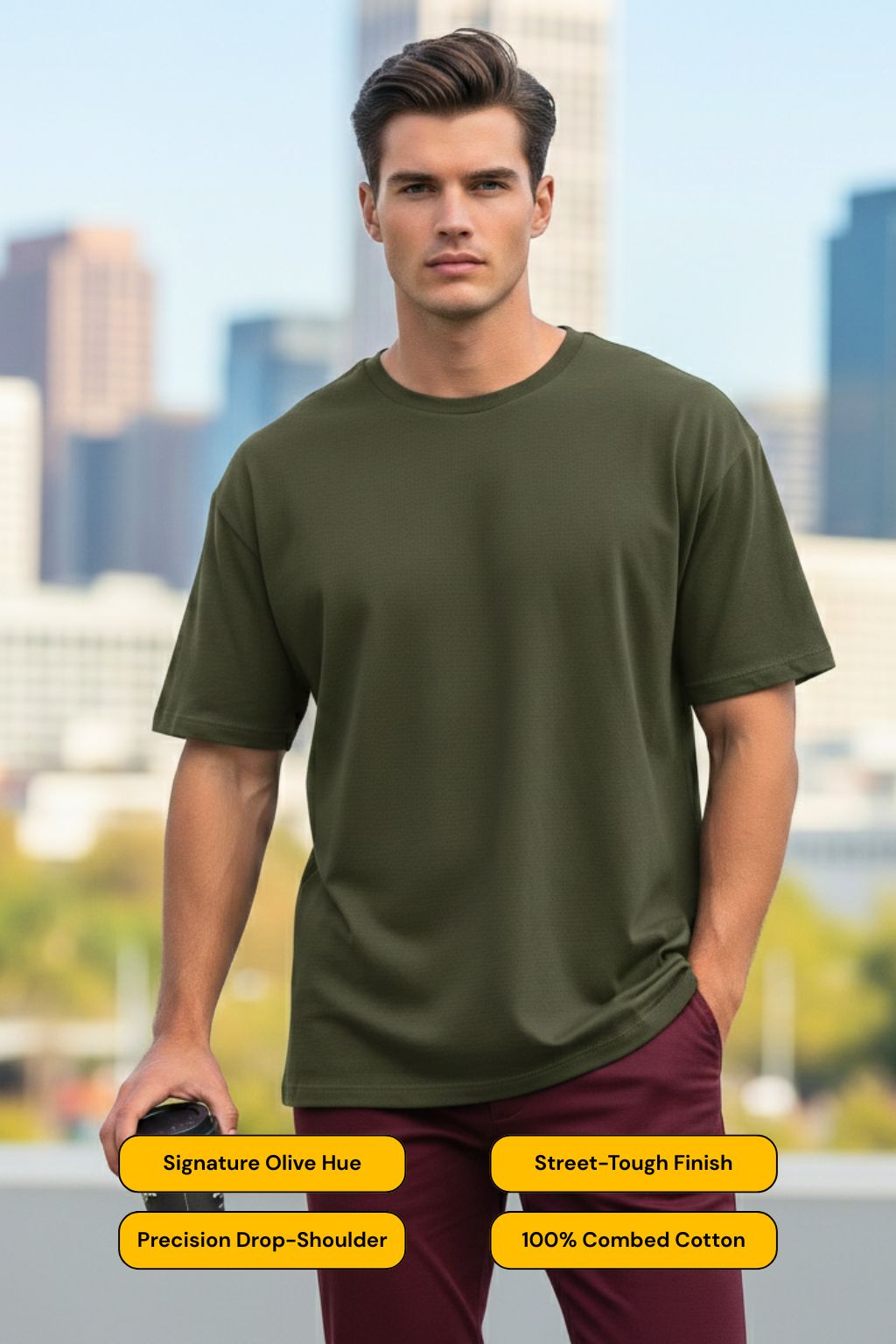 Man wearing a olive green oversized t-shirt with text detailing features, standing against a cityscape background.