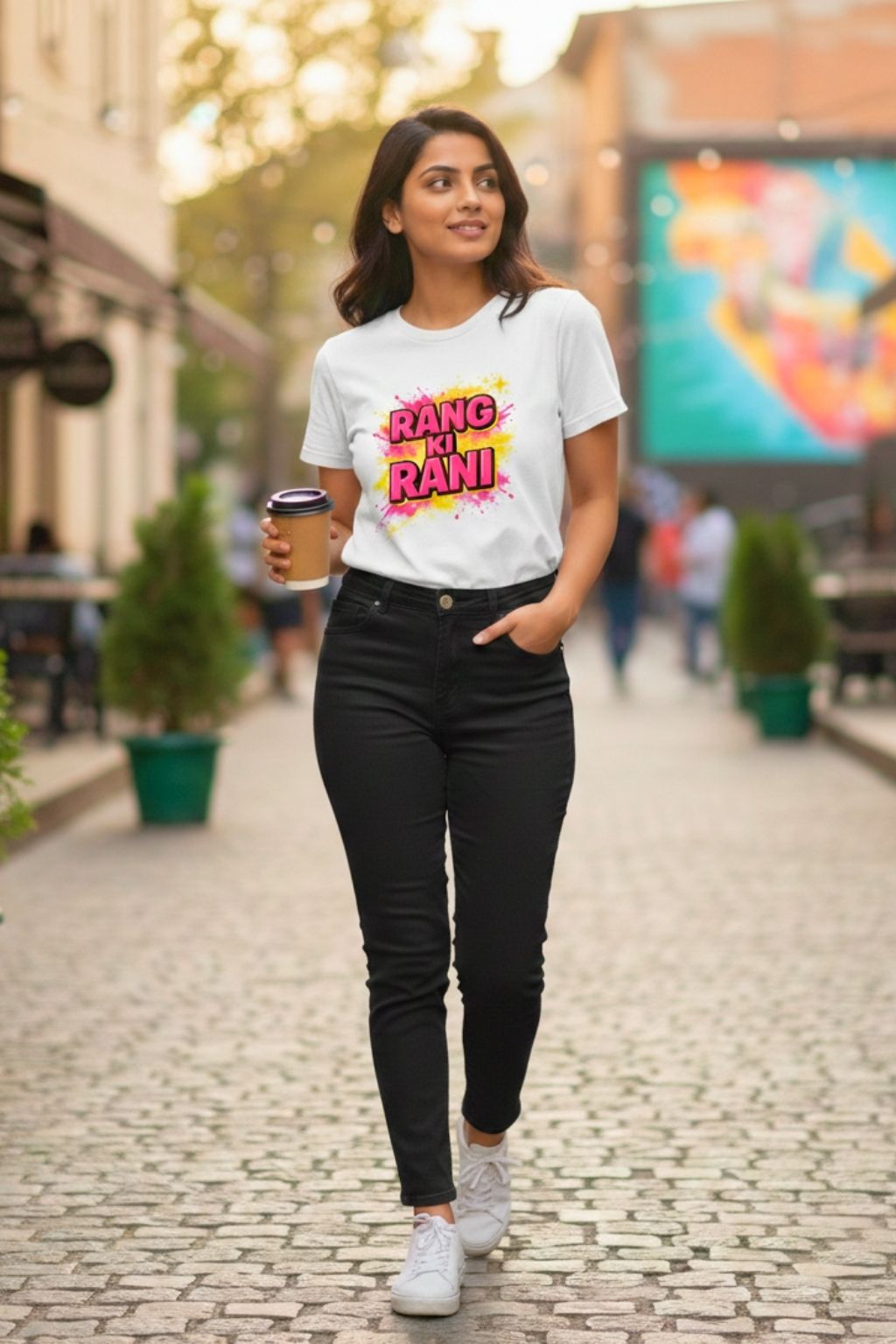 Woman walking on a street wearing a white t-shirt with colorful text "rang ki rani" and black jeans.