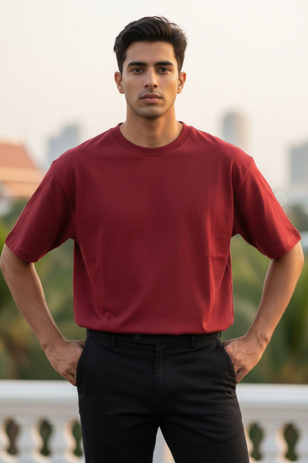 Man wearing a red oversized t-shirt and black pants standing outdoors with a blurred background