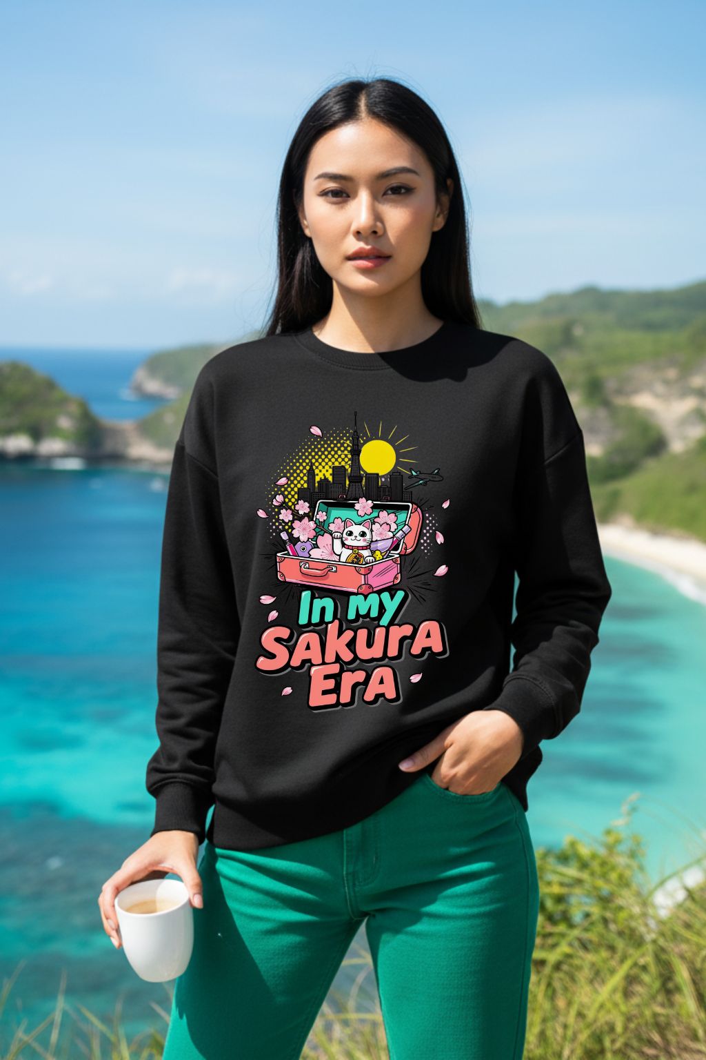 Woman wearing a black oversized sweatshirt with a colorful graphic and text, standing in front of a scenic ocean view.
