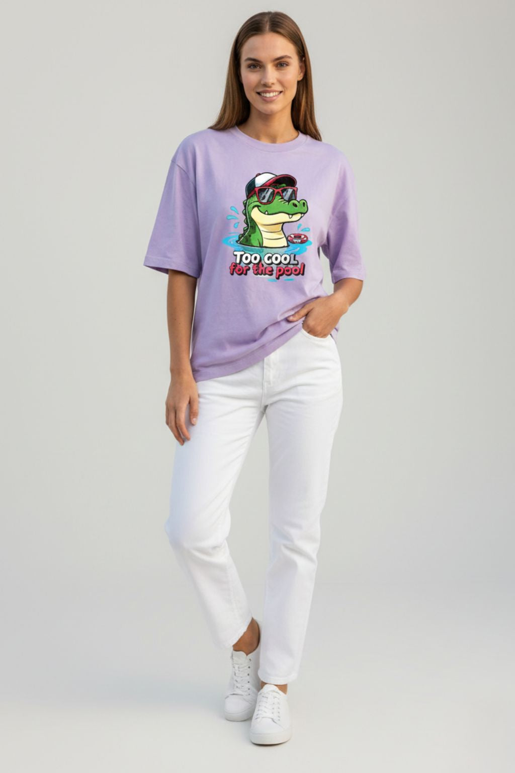 Woman wearing a lavendar oversized t-shirt with a graphic design of "too cool croc" on a plain background