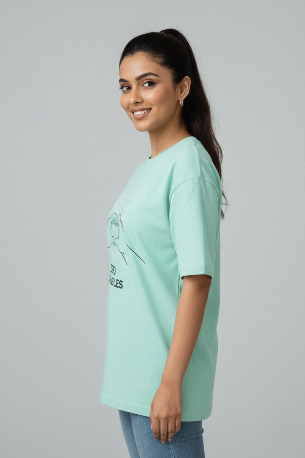side view of a woman wearing a mint oversized t-shirt with a design of "upsc aspirant zero variables" on a plain background
