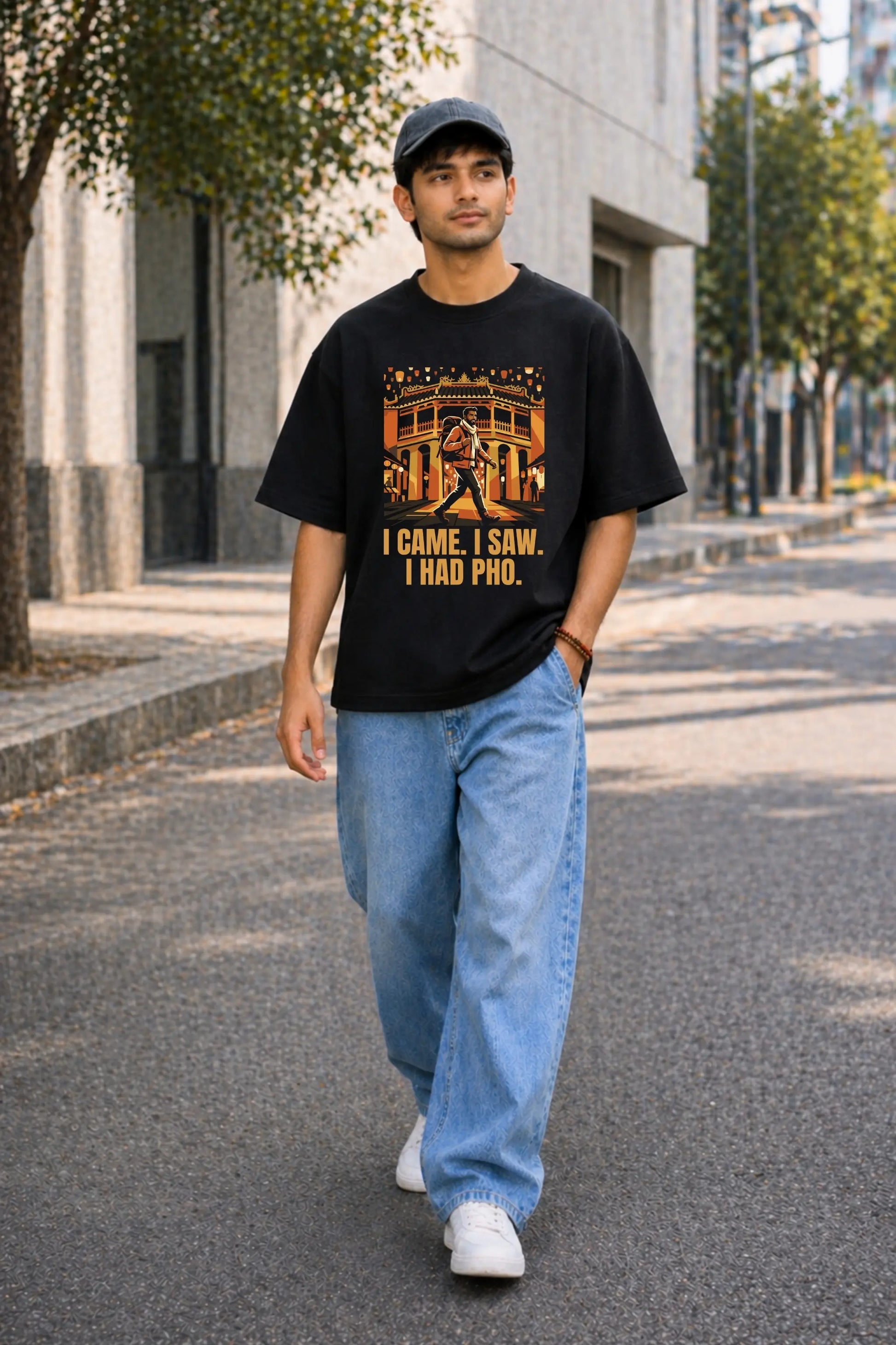 Indian man walking in black oversized Vietnam travel tee with bold amber Hội An graphic and I Came I Saw I Had Pho text, casual streetwear styling, JUNOSHI