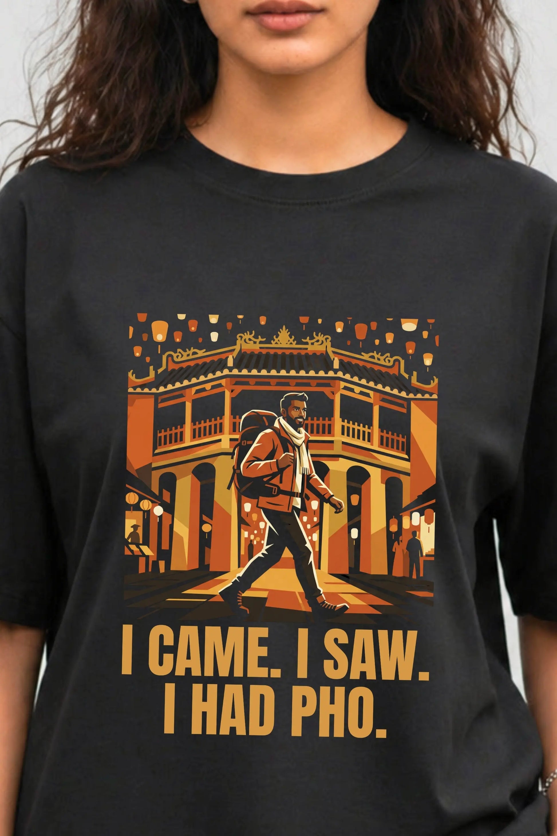 Close-up of black oversized tee featuring South Asian male traveler graphic at Hội An bridge with bold amber I Came I Saw I Had Pho text, JUNOSHI