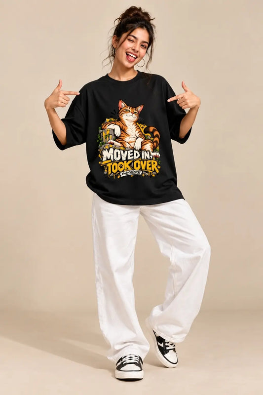 Woman wearing black Moved In Took Over Indie Cat oversized terry t-shirt with white wide-leg pants, pointing at the cat graphic | JUNOSHI