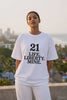A young Indian woman stands confidently on a Mumbai rooftop with the sea and city skyline behind her, wearing a white oversized tee printed with bold black text — 21, Life. Liberty. Mine. — from JUNOSHI's Written in Stone drop.