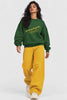 Model walking in Naan Thamizhachi Tamil pride oversized sweatshirt in bottle green with mustard wide-leg jeans | JUNOSHI
