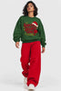 Model walking in Santa’s Favorite Girl bottle green oversized Christmas sweatshirt with red wide-leg jeans | JUNOSHI