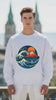 video of a man wearing a white oversized sweatshirt with a design of a wave with a mountain and sun in the background.