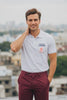 Young man wearing JUNOSHI Introvert Loading white polo t-shirt, standing on a rooftop with a relaxed confident expression, urban Indian cityscape in the background