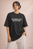 Young Indian woman wearing JUNOSHI's black oversized tee with the phrase "No Longer That. Not Yet This." printed in bold white text — part of the Unfiltered drop, for anyone mid-transition and honest about it.