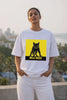 Woman wearing JUNOSHI Billi Boss white oversized tee featuring a bold black street cat illustration on electric yellow, styled with white pants against a Mumbai skyline backdrop